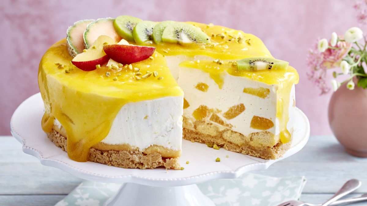 Tropische Tiramisu-Torte auf einem weißen Tortenteller vor einem rosa Hintergrund. Rechts auf dem Foto Blumen in einer rosa Vase.