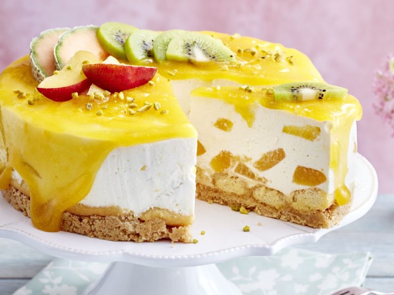 Tropische Tiramisu-Torte auf einem weißen Tortenteller vor einem rosa Hintergrund. Rechts auf dem Foto Blumen in einer rosa Vase.