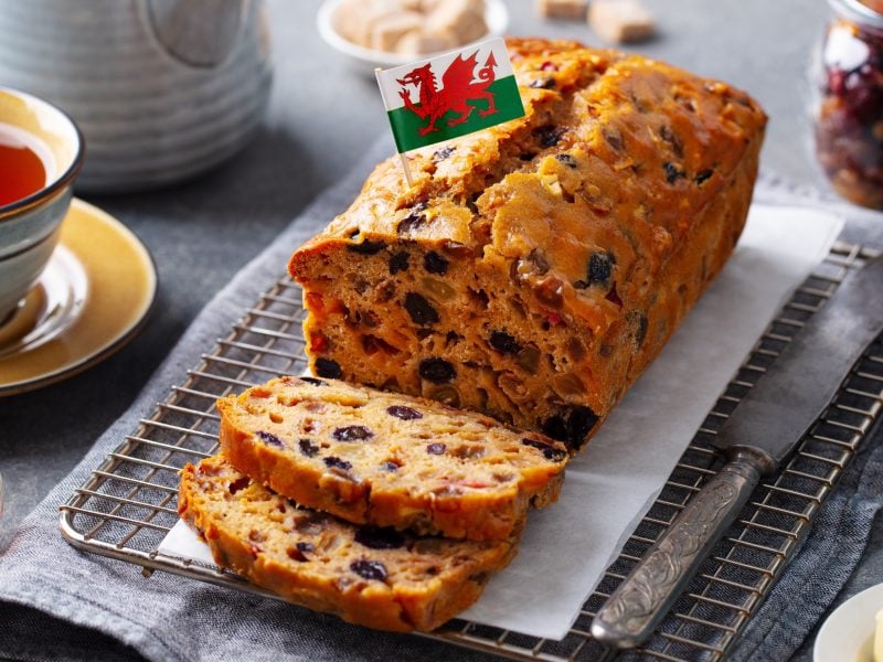 Draufsicht, schräg: Ein gedeckter Tisch mit einer Tasse Tee, Marmelade und einem aufgeschnittenen Früchtebrot Bara Brith aus Wales.