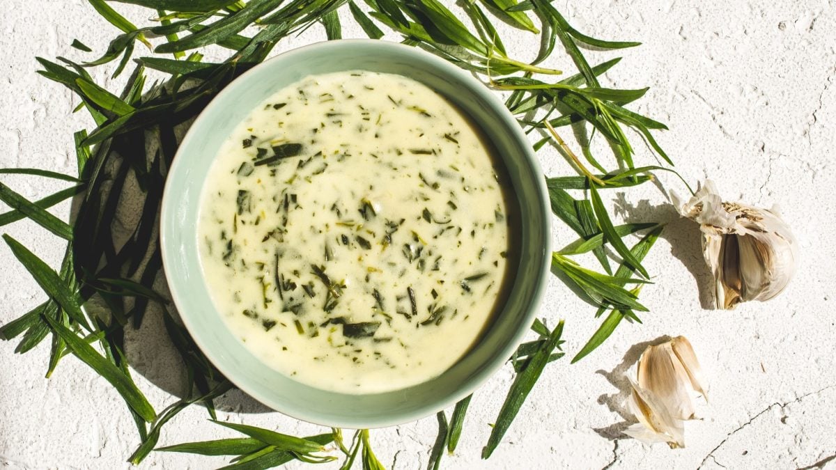 Draufsicht: heller Untergrund, runde Schüssel mit einer hellen Sauce und Kräutern. Drum herum frische Kräuter verteilt.