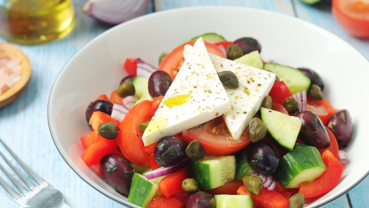 Draufsicht schräg: eine hellerunde Schüssel. In der ist ein griechischer Bauernsalat mit Feta.