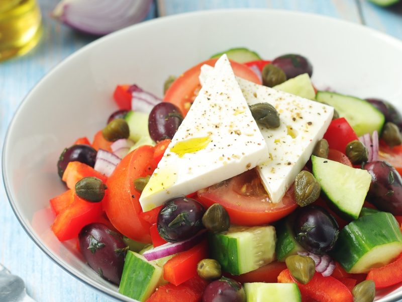 Draufsicht schräg: eine hellerunde Schüssel. In der ist ein griechischer Bauernsalat mit Feta.