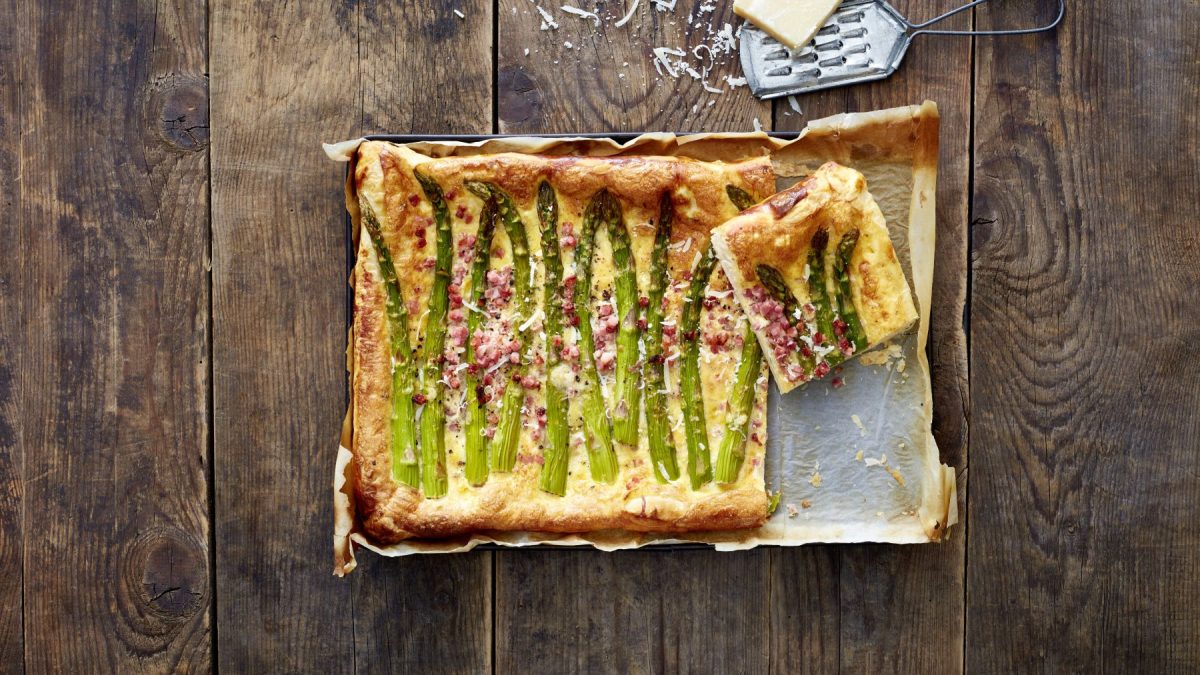 Specktakuläre Carbonara-Spargel-Crostata auf einem Blech auf hölzernem Hintergrund.