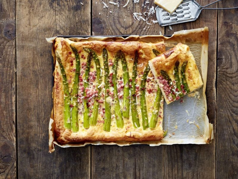 Specktakuläre Carbonara-Spargel-Crostata auf einem Blech auf hölzernem Hintergrund.