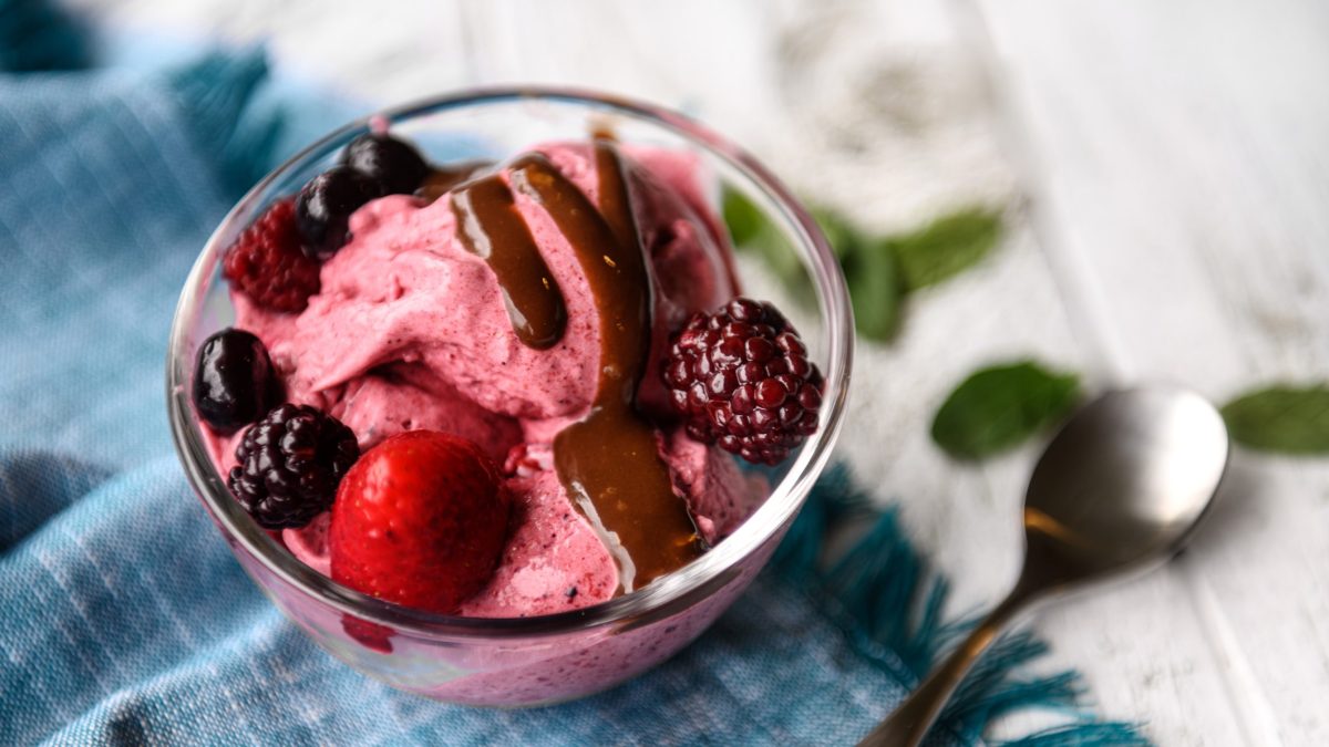 Draufsicht: ein Glas mit mehreren Kugeln Hüttenkäse-Eis und frischen beeren. Daneben liegen ein Löffel und zwei Tücher.