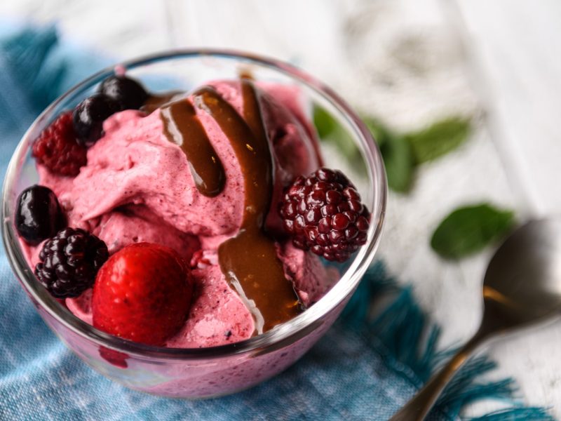 Draufsicht: ein Glas mit mehreren Kugeln Hüttenkäse-Eis und frischen beeren. Daneben liegen ein Löffel und zwei Tücher.