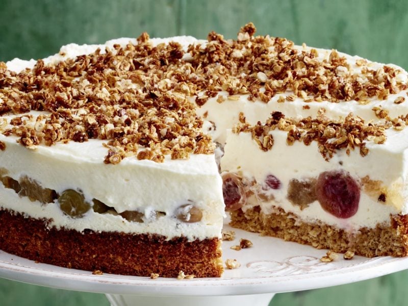 Stachelbeer-Torte mit Haferflocken-Crunch auf einem weißen Tortenteller vor grünem Hintergrund.