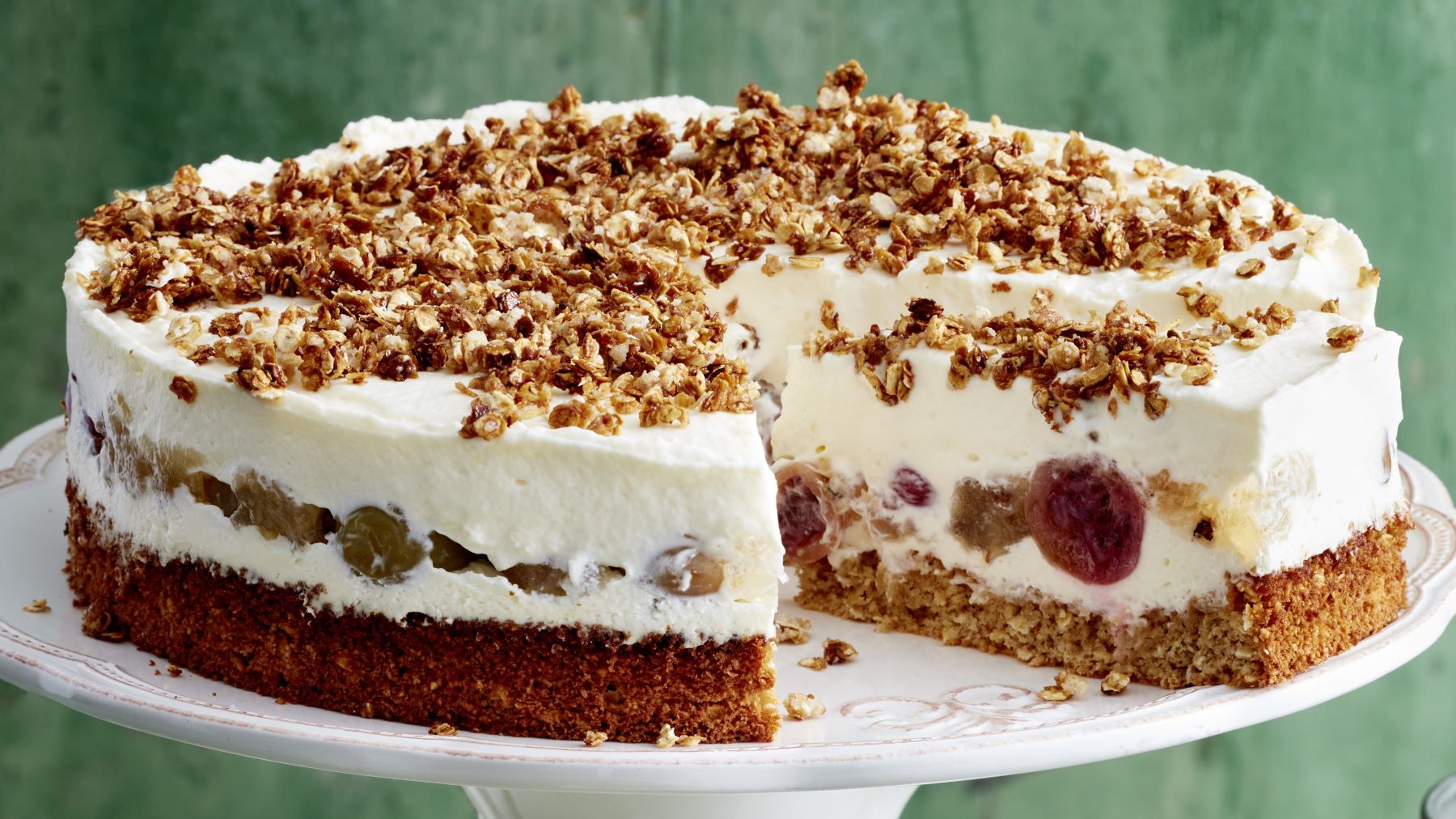 Stachelbeer-Torte mit Haferflocken-Crunch auf einem weißen Tortenteller vor grünem Hintergrund.