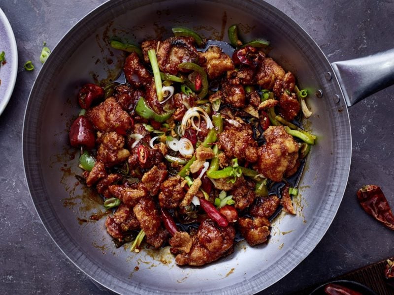 Sticky Chilichicken mit Knusperstrippen in einer Gusseisenpfanne auf silbernem Hintergrund.