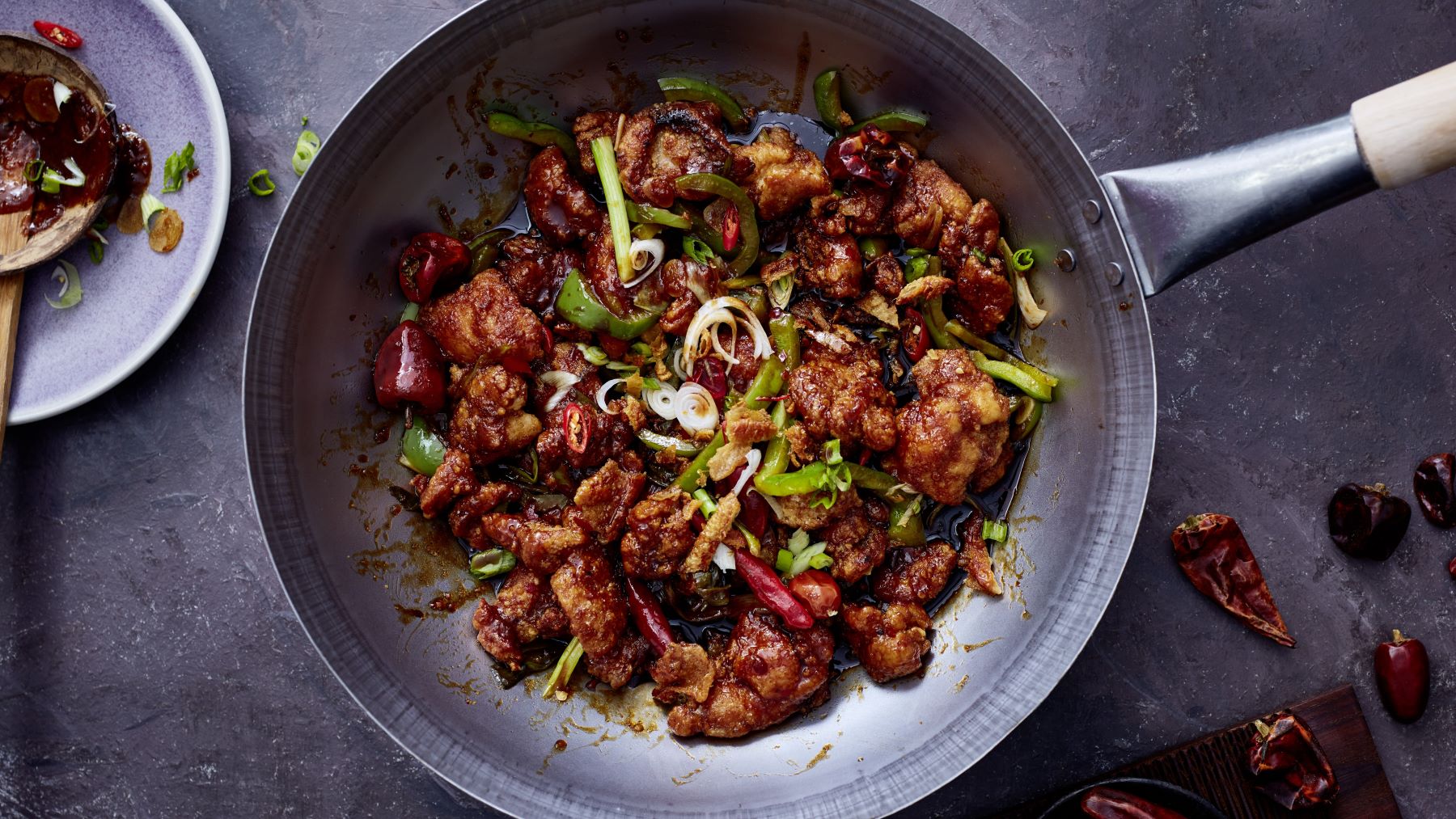 Sticky Chilichicken mit Knusperstrippen in einer Gusseisenpfanne auf silbernem Hintergrund.