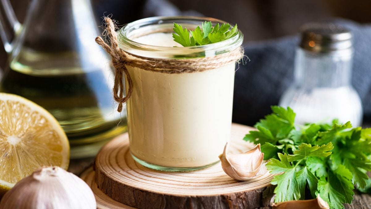 Frontal: Ein Gefäß aus Glas mit einer hellen Creme, eine halbe Zitrone und ein Gefäß mit Öl. Dunkler Hintergrund.