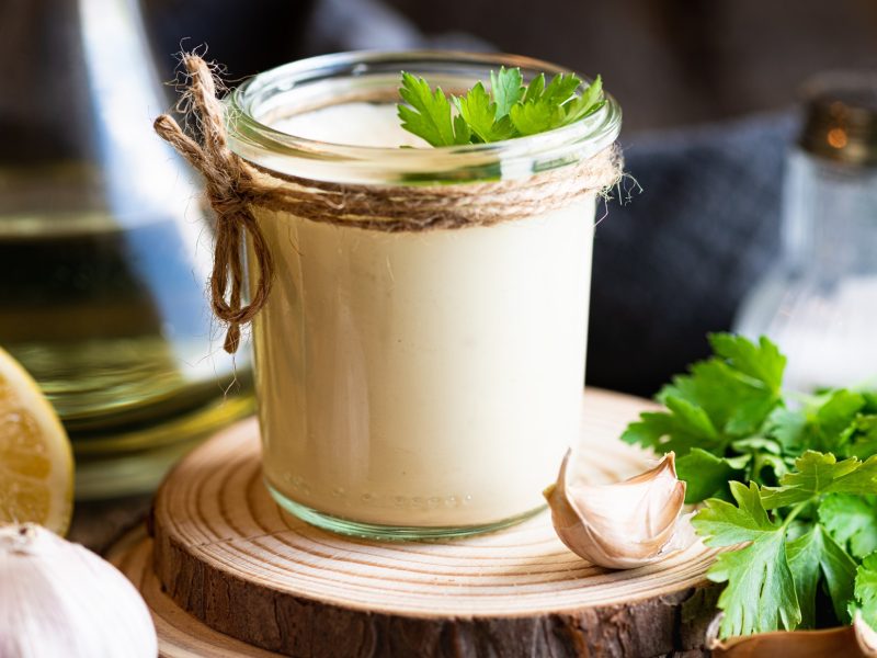 Frontal: Ein Gefäß aus Glas mit einer hellen Creme, eine halbe Zitrone und ein Gefäß mit Öl. Dunkler Hintergrund.