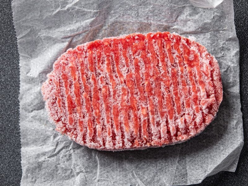Draufsicht: Hackfleisch, gefroren, ovales Patty auf hellem Papier auf dunklem Untergrund.