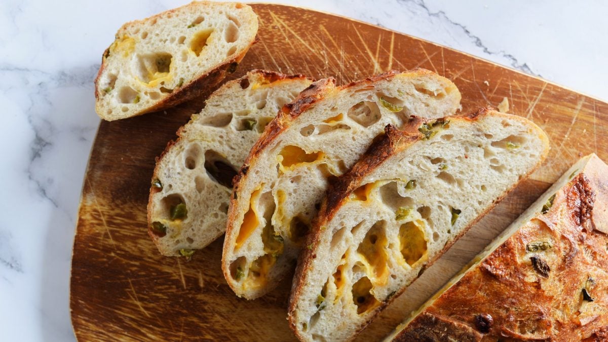 Fünf Scheiben knuspriges Sauerteigbrot mit geschmolzenem Cheddar und Jalapeños auf einem angerauten Holzbrett.