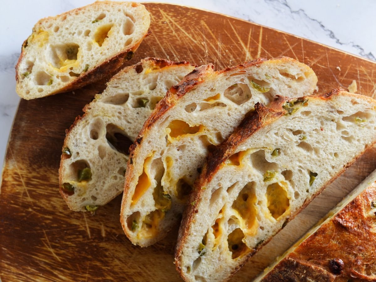Fünf Scheiben knuspriges Sauerteigbrot mit geschmolzenem Cheddar und Jalapeños auf einem angerauten Holzbrett.