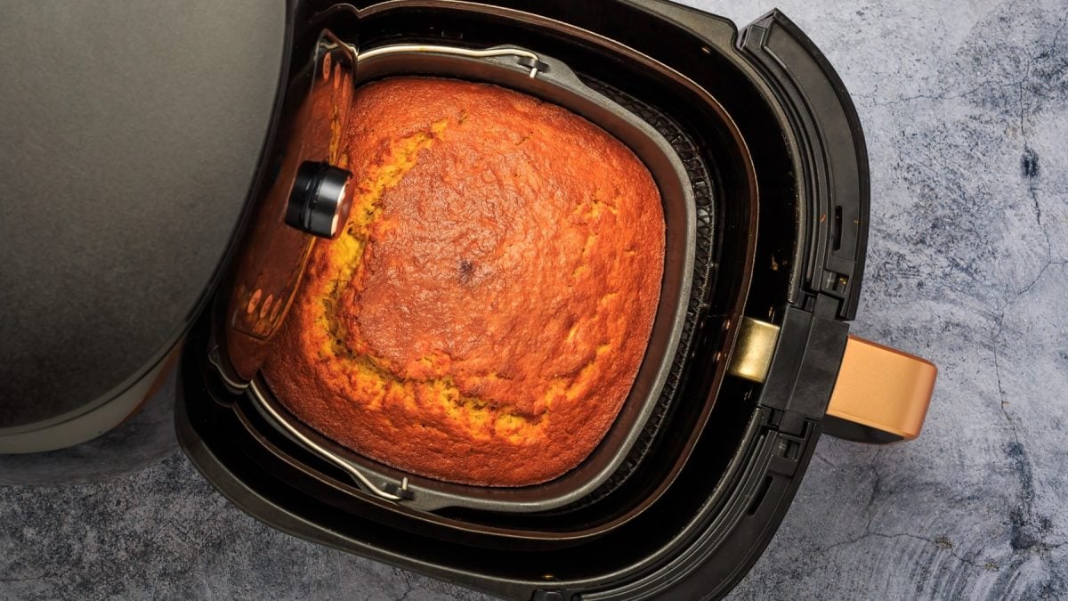 Ein Airfryer mit dem Kuchen auf einem Marmortisch. Alles direkt von oben fotografiert.