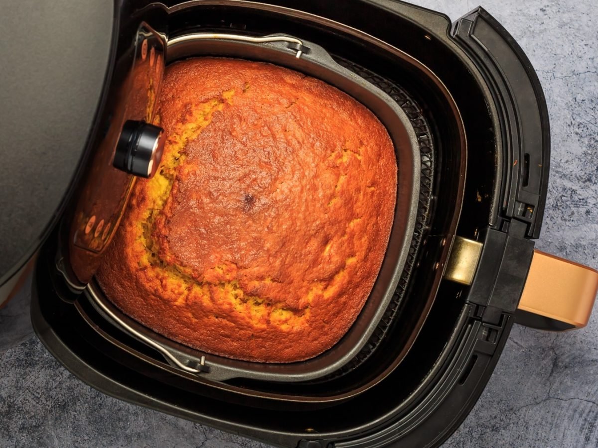 Ein Airfryer mit dem Kuchen auf einem Marmortisch. Alles direkt von oben fotografiert.