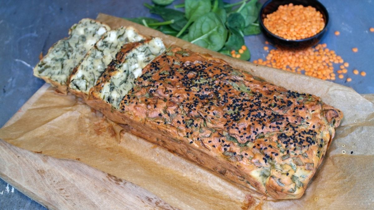 Das angeschnittene Linsenbrot auf einem Holzbrett mit Backpapier. Alles auf einem grauen Steintisch.