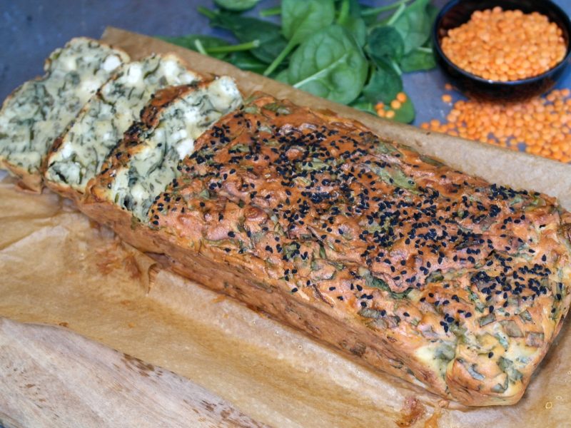 Das angeschnittene Linsenbrot auf einem Holzbrett mit Backpapier. Alles auf einem grauen Steintisch.