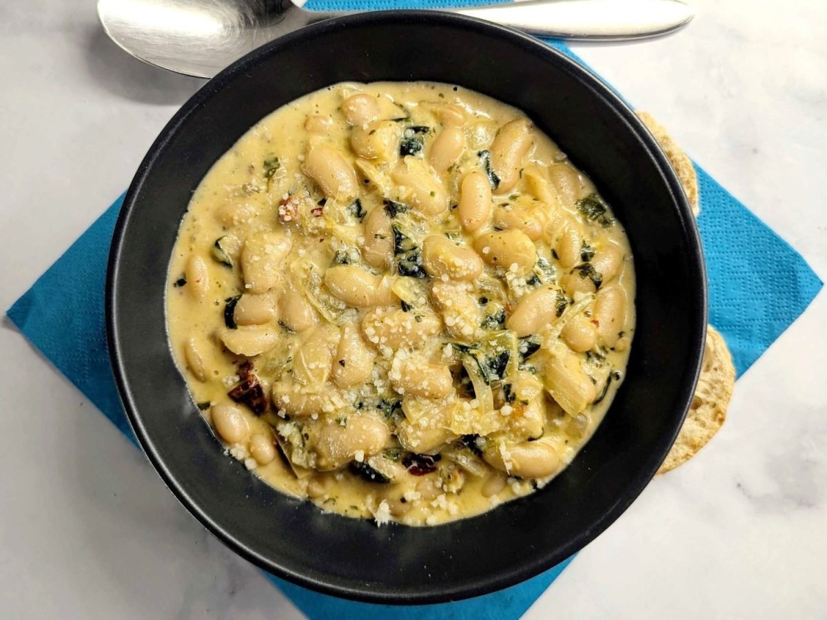 Schwarzer Teller auf weißem Marmor. Darauf cremige Marry Me Beans in cremiger Sauce.