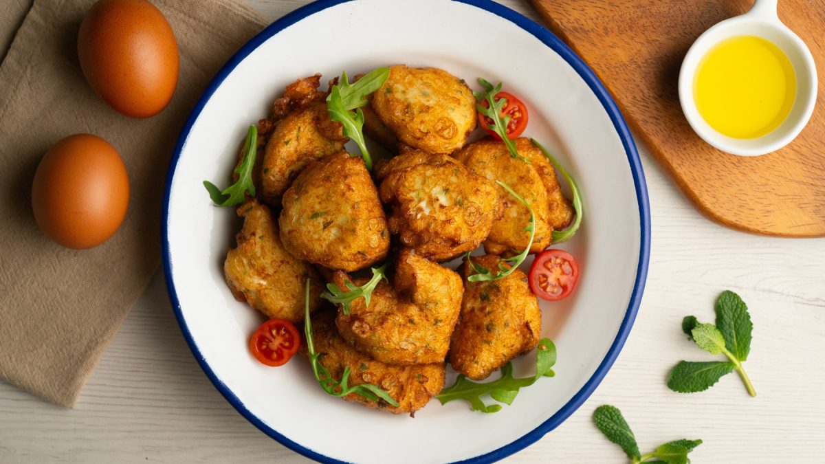 Goldbraune Parpuchas auf weißem Teller mit Rucola und Cherrytomaten, daneben zwei Eier und frische Minze.