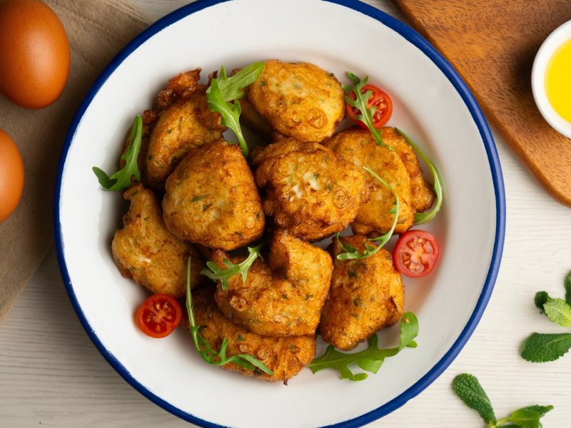 Goldbraune Parpuchas auf weißem Teller mit Rucola und Cherrytomaten, daneben zwei Eier und frische Minze.