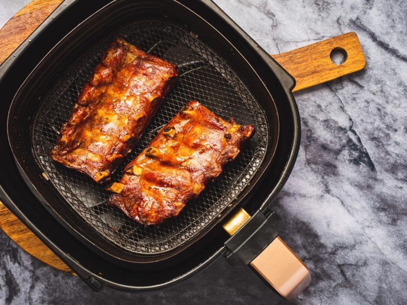 Zwei Stücke Spare Ribs im Airfryer auf einem Marmortisch direkt von oben fotografiert.