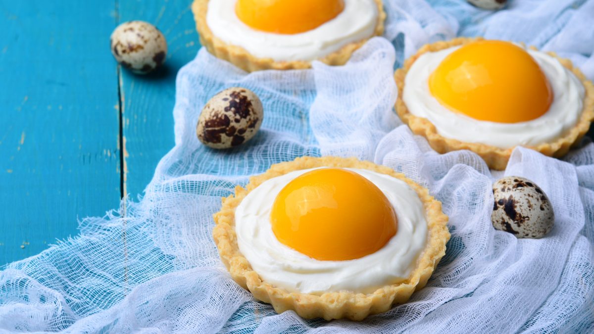 Drei Tartelettes mit Aprikose auf einem hellblauen Tisch mit Wachteleiern dekoriert.