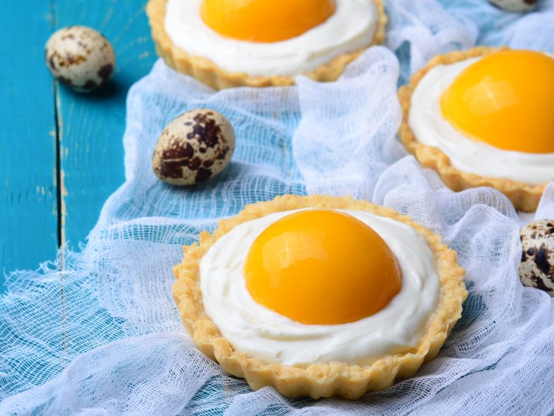 Drei Tartelettes mit Aprikose auf einem hellblauen Tisch mit Wachteleiern dekoriert.
