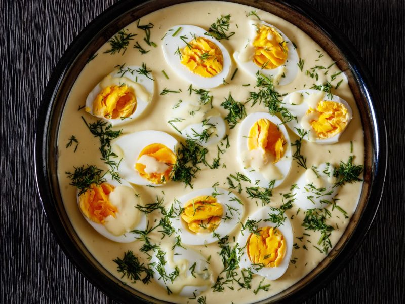 Hart gekochte Eier in cremiger Sauce mit Kräuterdekor, angerichtet in einer schwarzen Bowl mit mattem Finish.