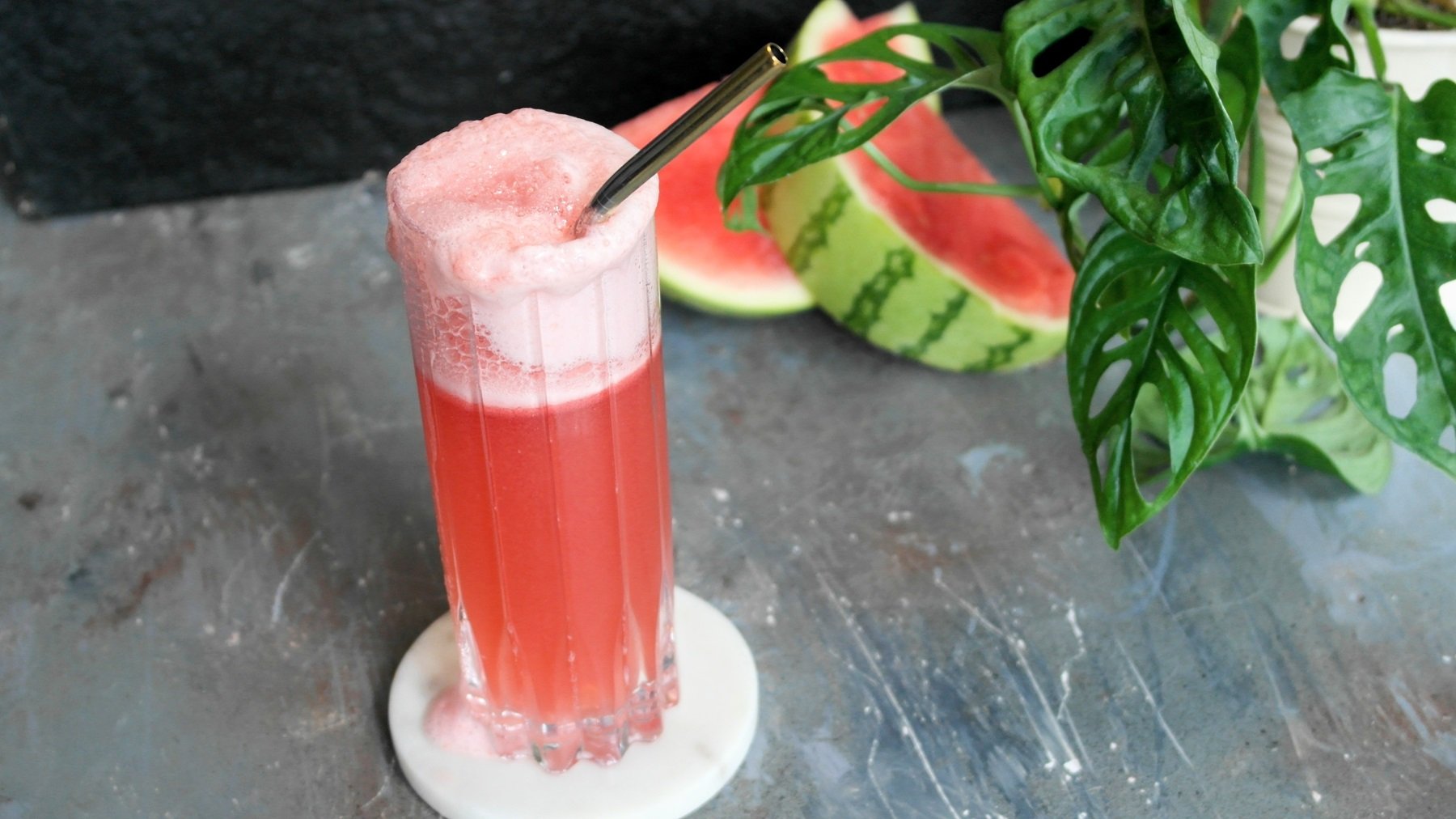 Ein Glas mit dem roten Cocktail auf einem grauen Untergrund. Alles von schräg oben fotografiert.