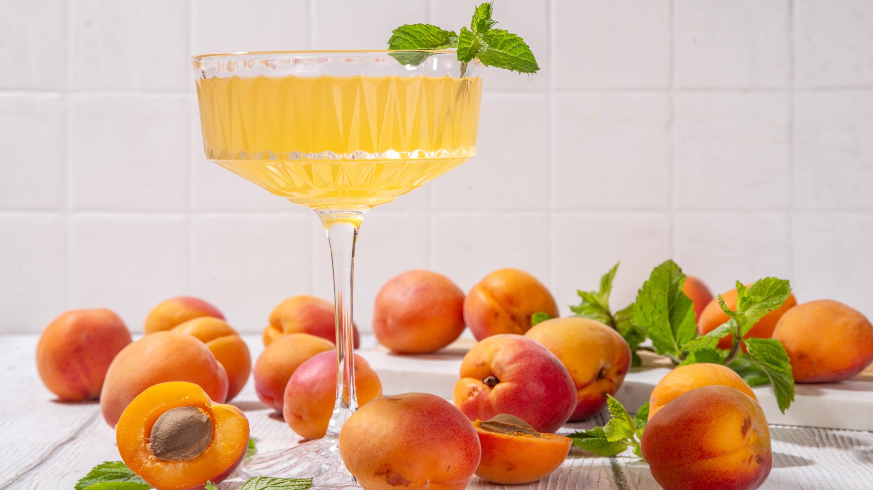 Aprikosen-Mandarinen-Martini in einem eleganten Cocktailglas umgeben von frischen und angeschnittenen Aprikosen.