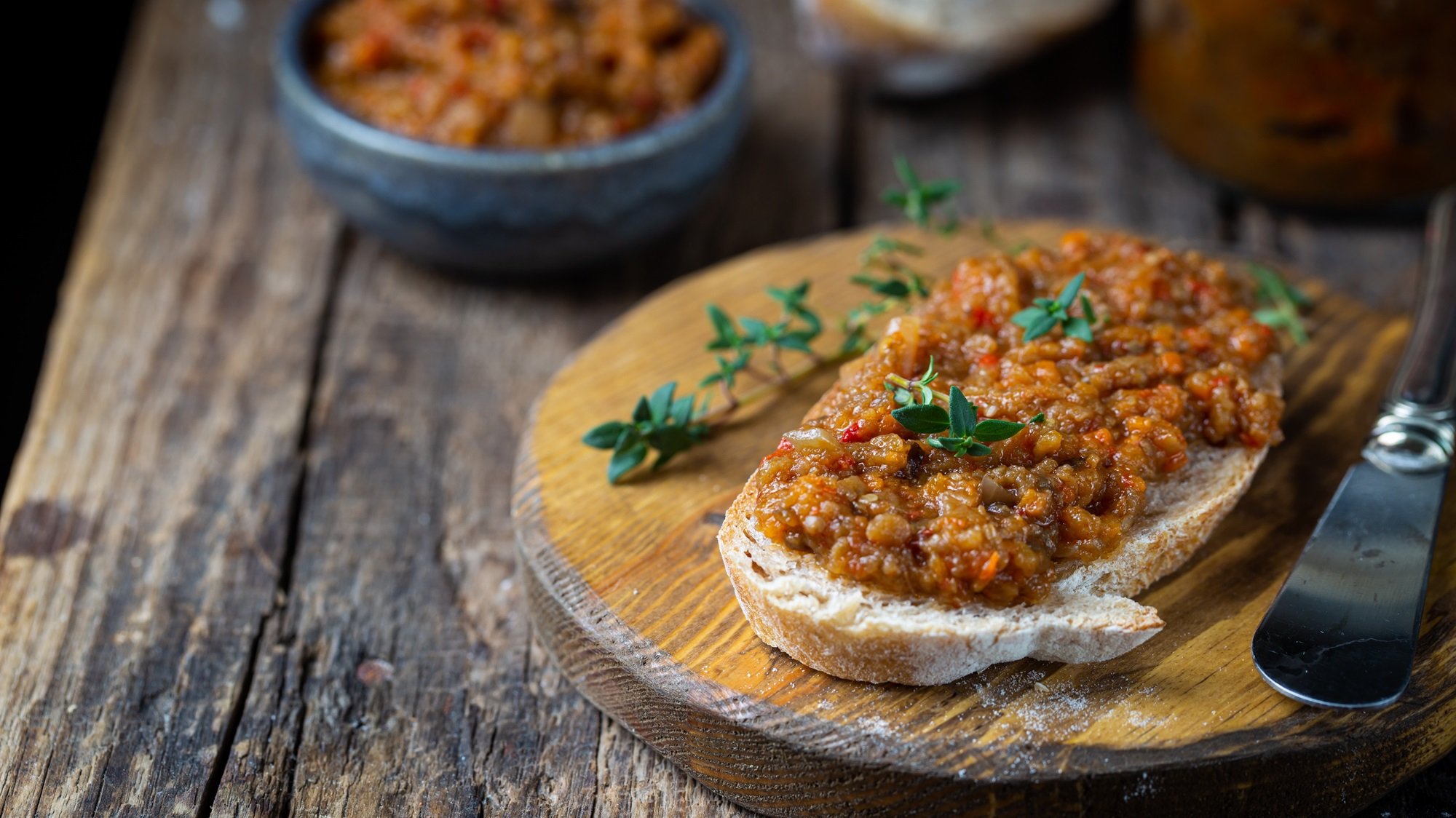 Geröstete Brotscheibe mit Auberginen-Kaviar und Thymianzweigen auf rustikalem Holzbrett bei natürlichem Licht.
