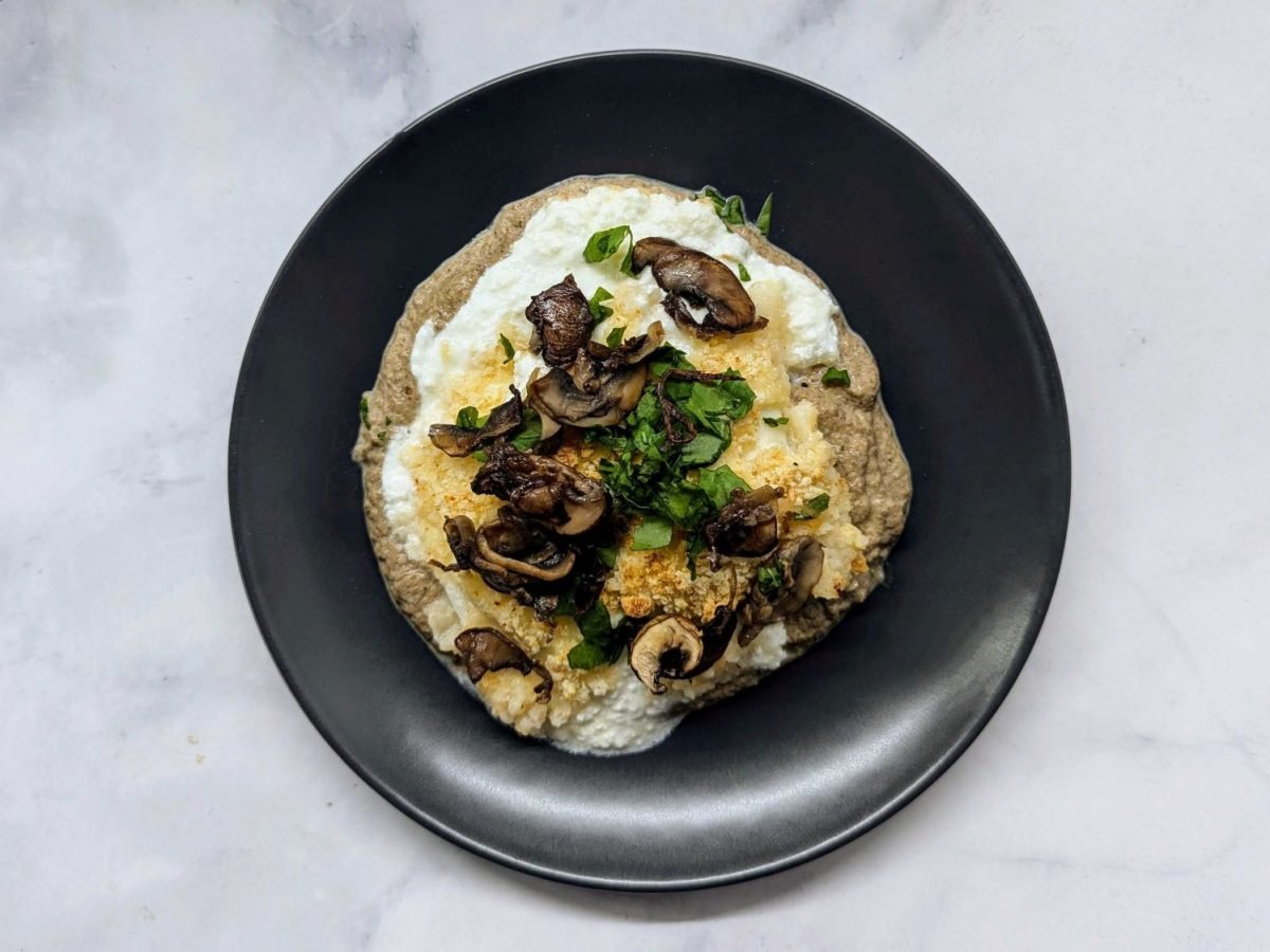 Burrata mit Champignons, frischer Petersilie und knusprigem Topping auf herzhafter Creme, serviert auf schwarzem Teller.