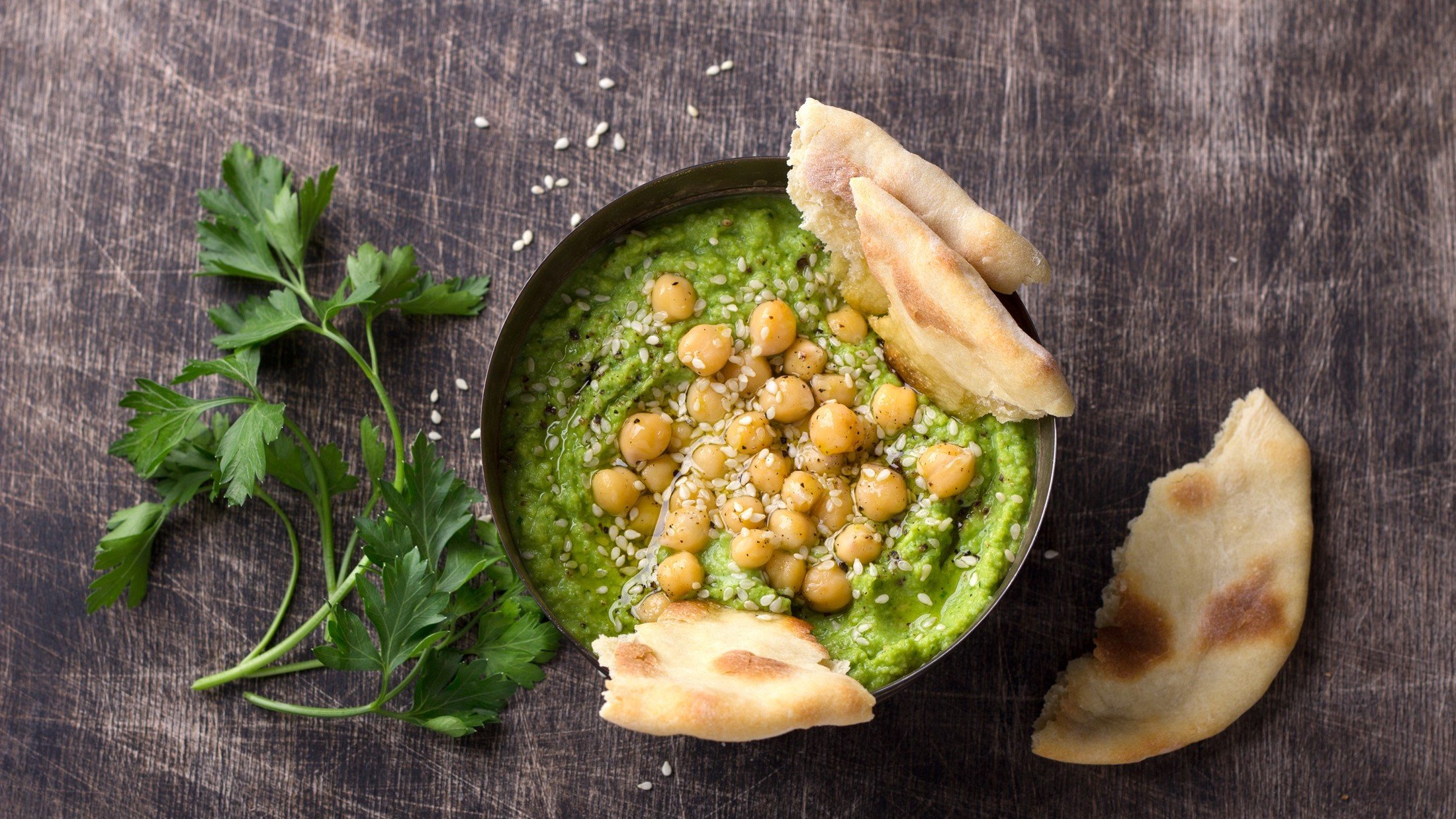 Green Goddess Hummus in einer dunklen Schüssel. / Fladenbrot zerrupft/