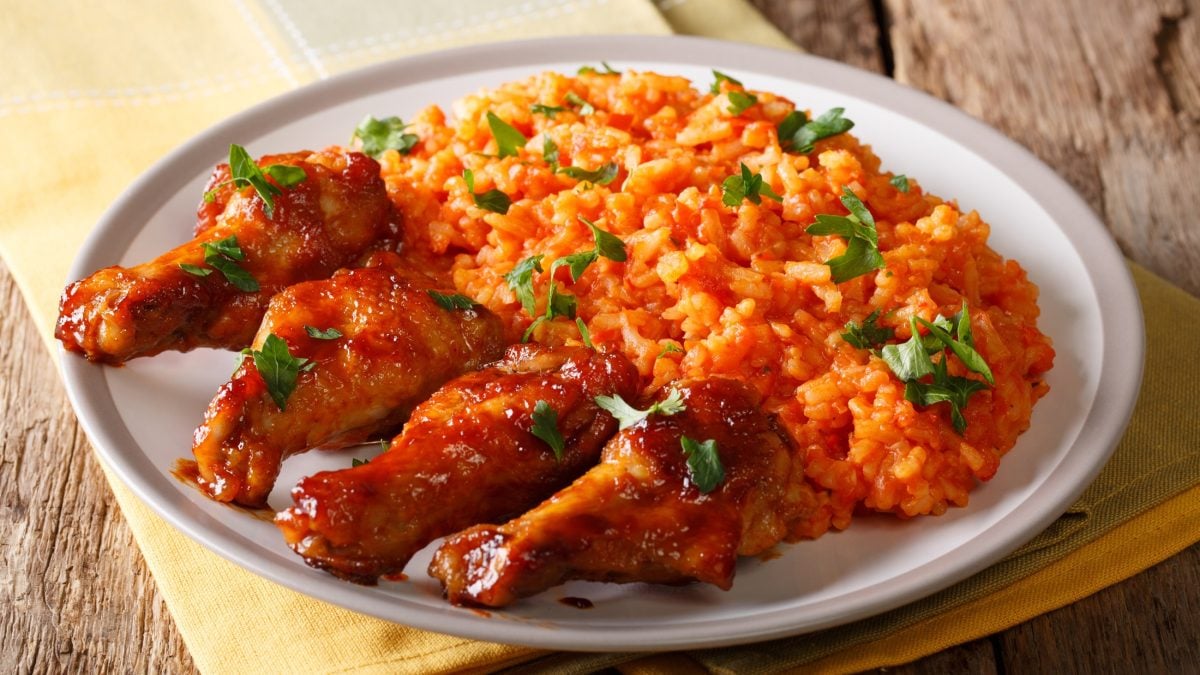 Jollof-Reis mit gebraten Hähnchenschenkeln auf einem runden Teller / Draufsicht, schräg