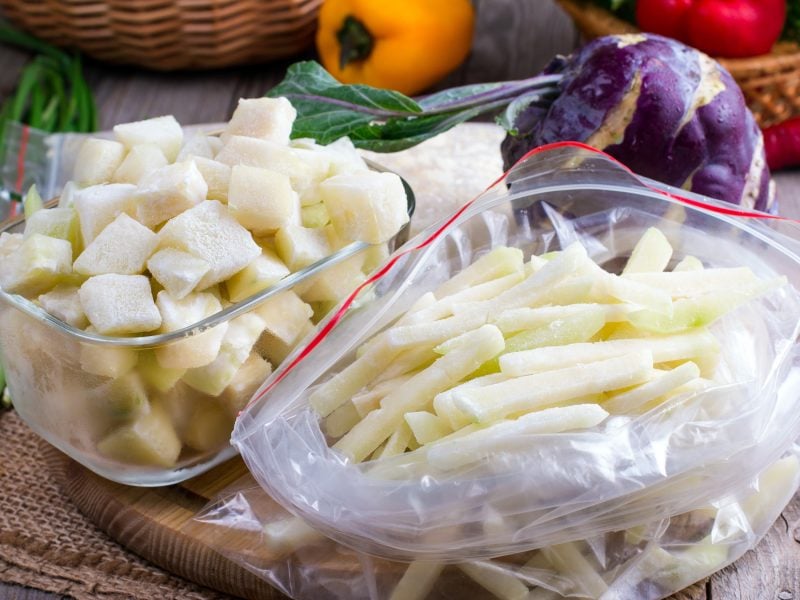 Draufsicht: Eingefrorener Kohlrabi, in Stifte und Würfel geschnitten, in verschiedenen Behältern. Im Hintergrund ist anderes Gemüse.