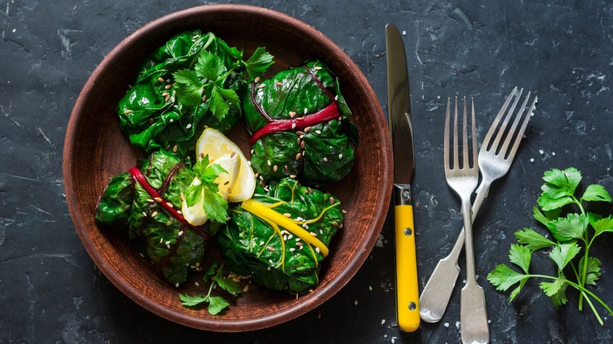 Vier Mangold-Rouladen mit Feta in einer runden schale. / Besteck / Frische Petersilie