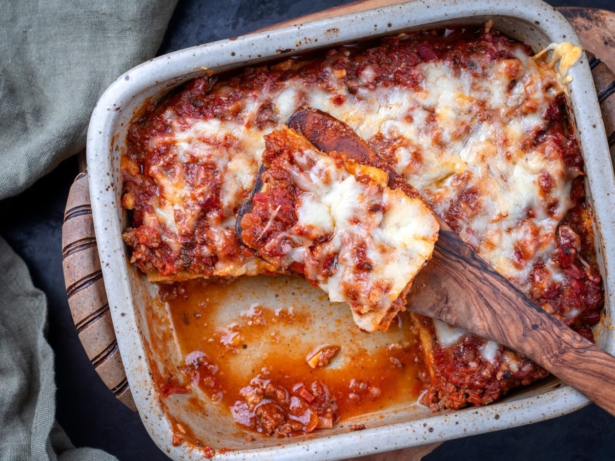 Ein ofenfeste Form mit einer Polenta mit Salsiccia. In dersteckt ein großer Löffel aus Holz / Draufsicht