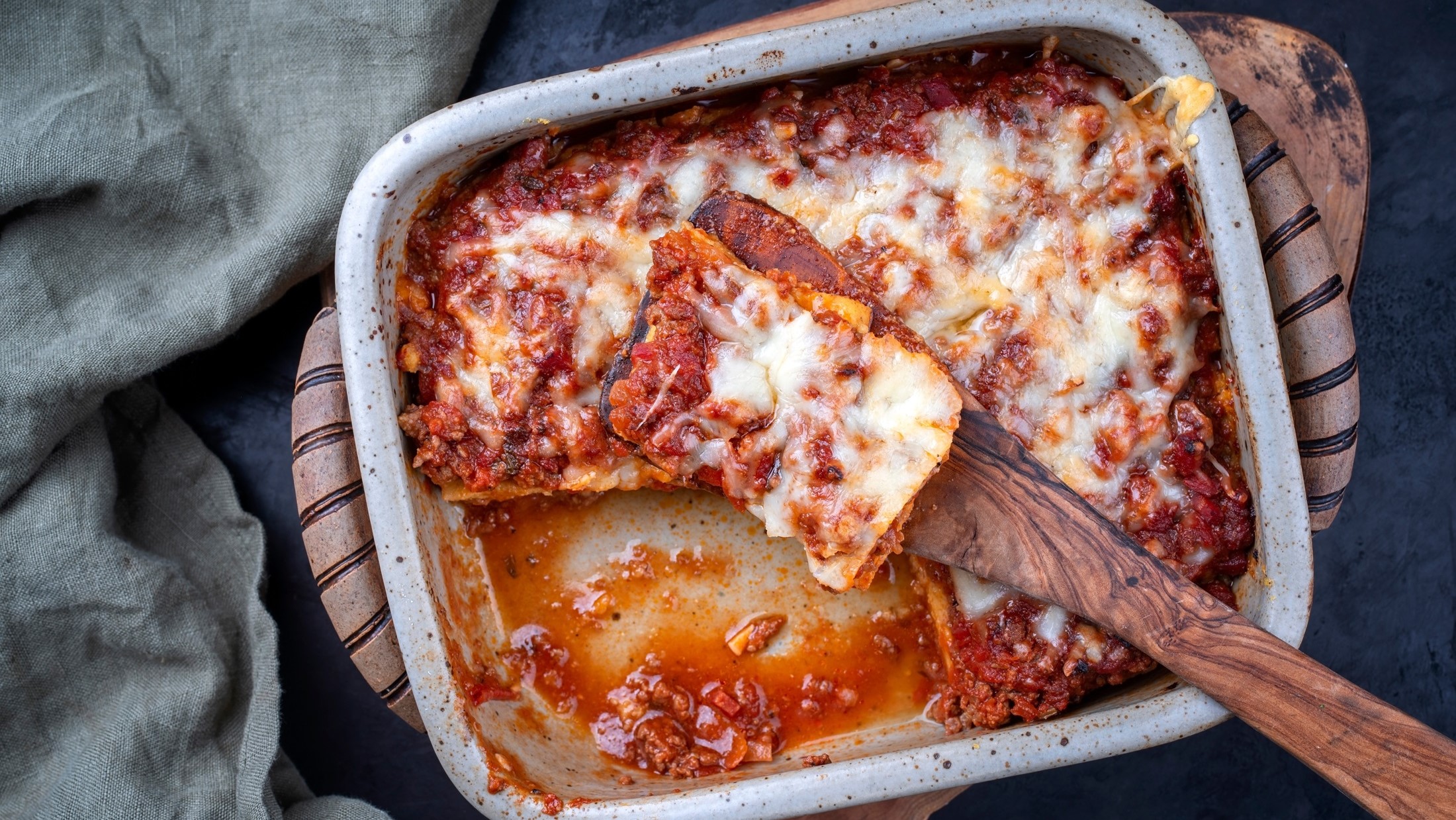 Ein ofenfeste Form mit einer Polenta mit Salsiccia. In dersteckt ein großer Löffel aus Holz / Draufsicht