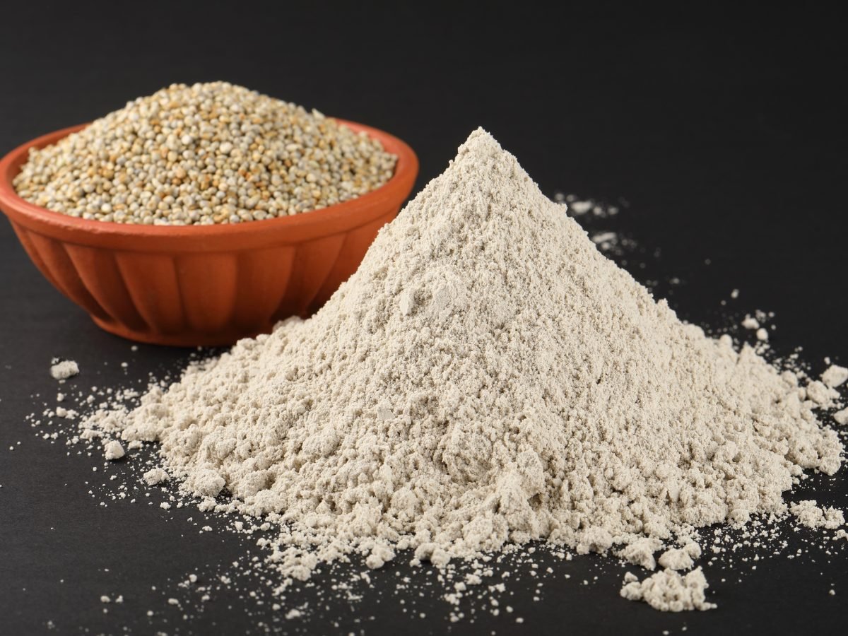 Frontal: Dunkler Untergrund, eine Schale mit Sorghum-Körnern und glutenfreies Sorghum-Mehl auf einem dunklen Untergund.