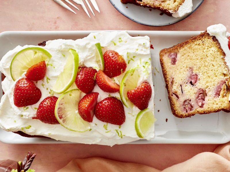Erdbeer-Holunderkuchen auf einem weißen Teller vor rosa Hintergrund.
