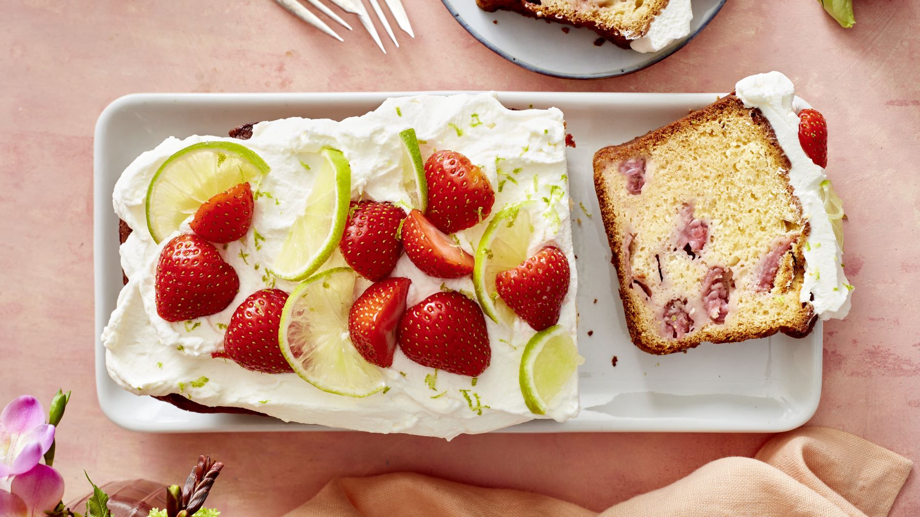 Erdbeer-Holunderkuchen auf einem weißen Teller vor rosa Hintergrund.