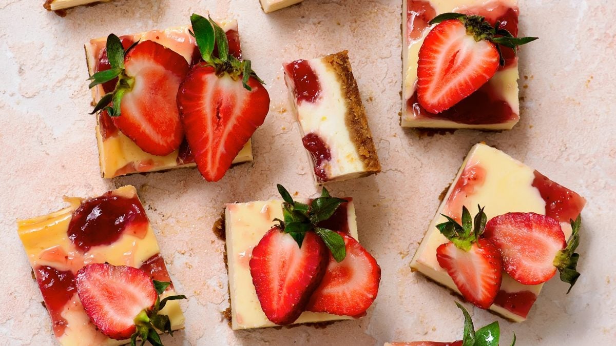 Erdbeer-Käsekuchen vom Blech mit glänzender Fruchtschicht und frischen Erdbeerhälften auf rustikalem, hellem Steintisch angerichtet.