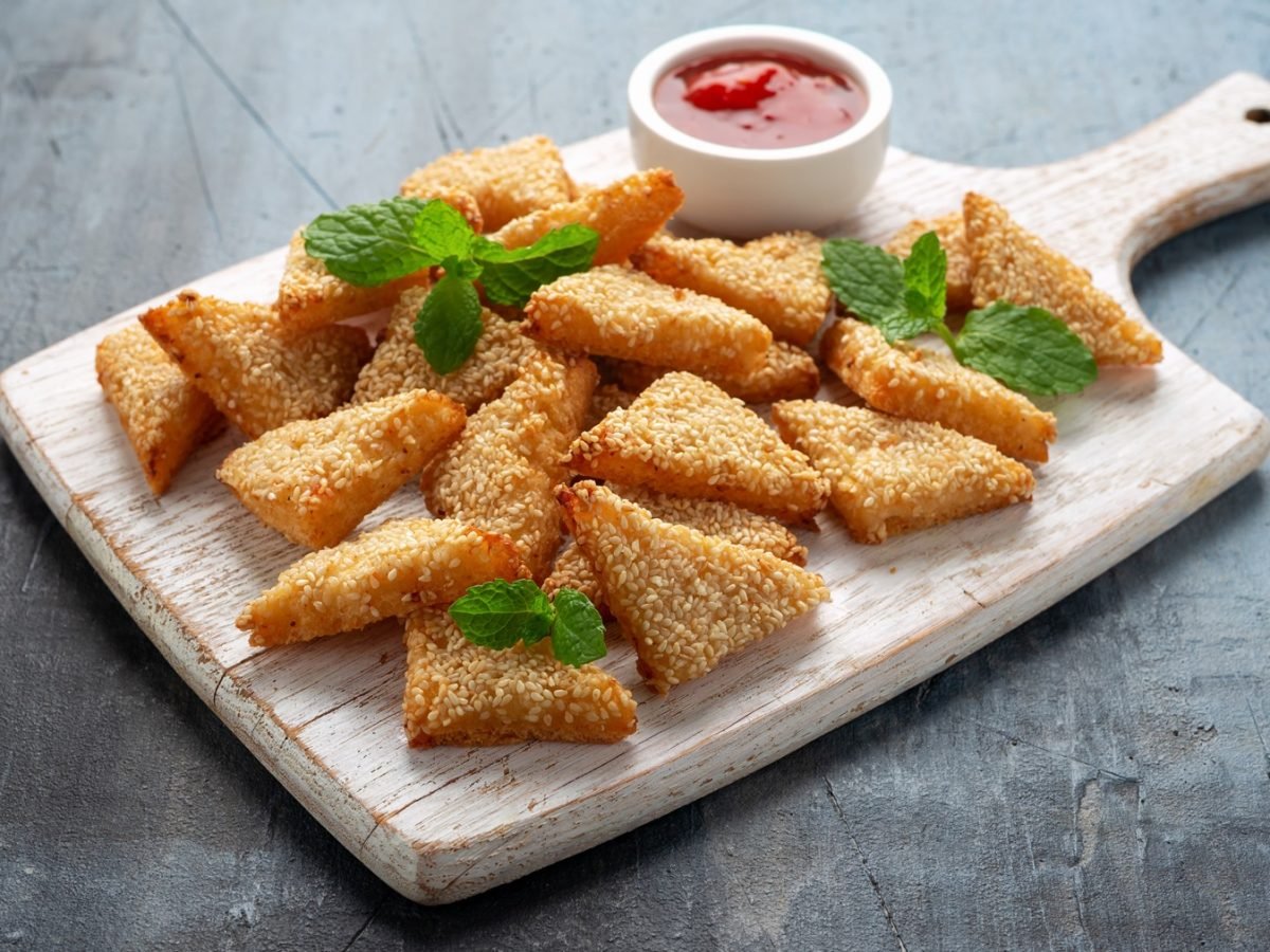 Ein Holzbrett mit den Granelen-Toasts auf einem grauen Tisch mit einem kleinen weißen Schälchen roter Sauce.