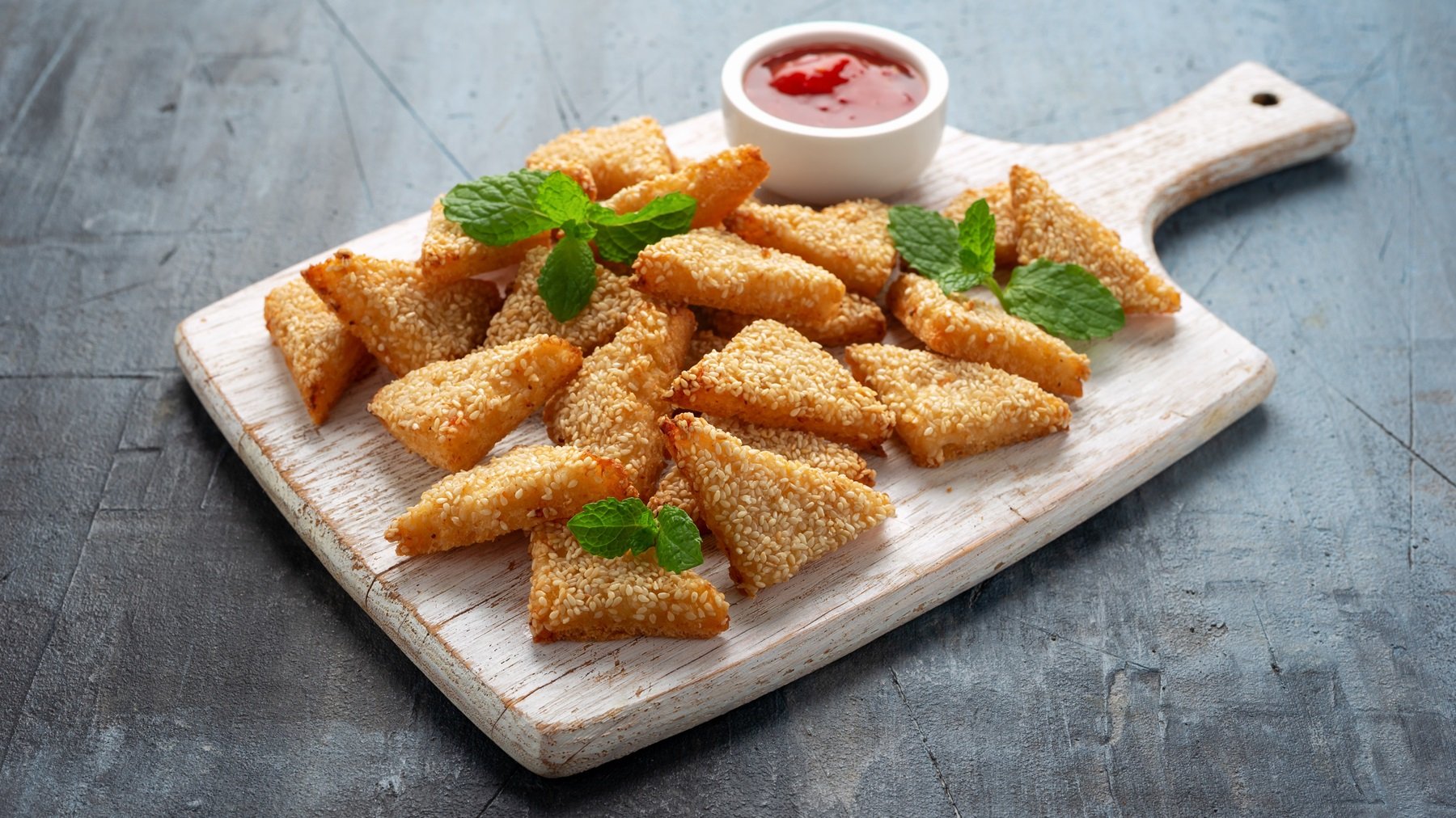 Ein Holzbrett mit den Granelen-Toasts auf einem grauen Tisch mit einem kleinen weißen Schälchen roter Sauce.