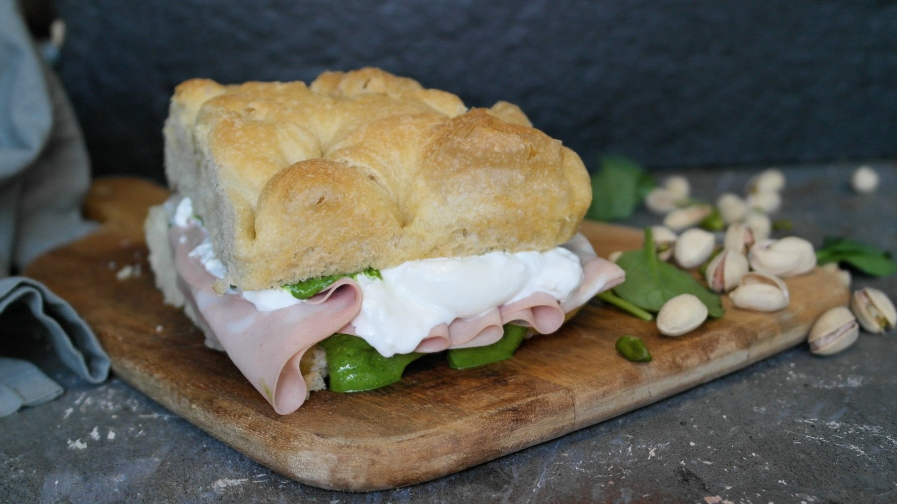 Das Sandwich auf einem Holzbrett und grauem Tisch von der Seite fotografiert.