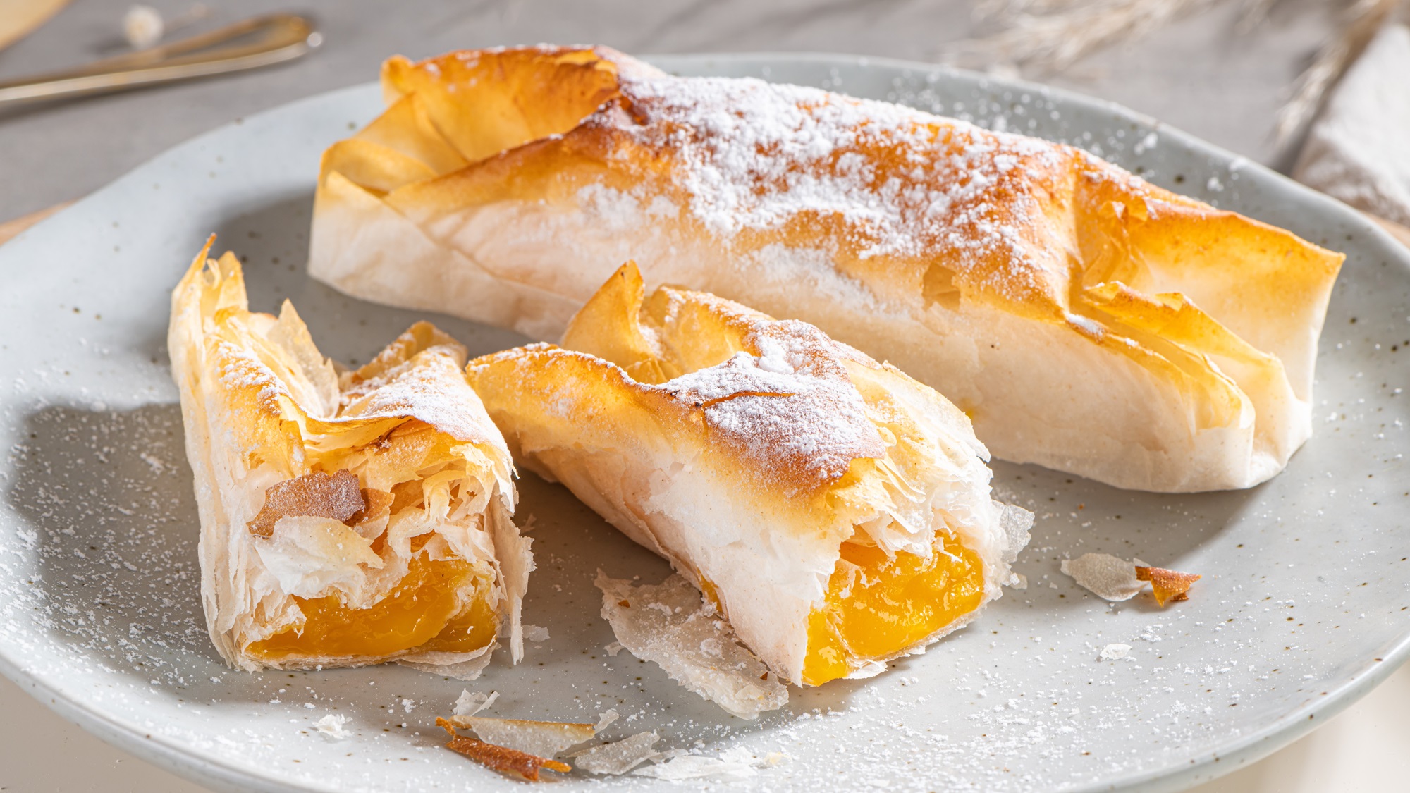 Knusprige Pasteis de Vouzela mit cremiger Eierfüllung auf einem grauen Keramikteller, bestäubt mit feinem Puderzucker im Tageslicht.