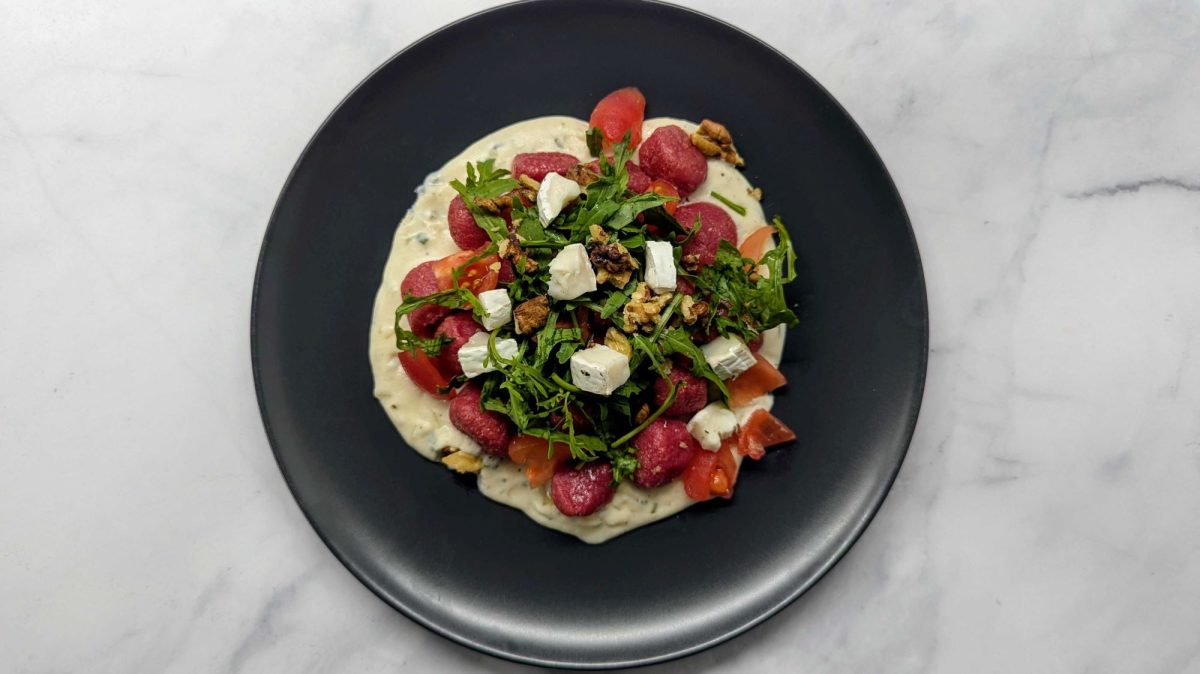 Rote-Bete-Gnocchi mit Frischkäse-Sauce und Rucola auf schwarzem Teller.