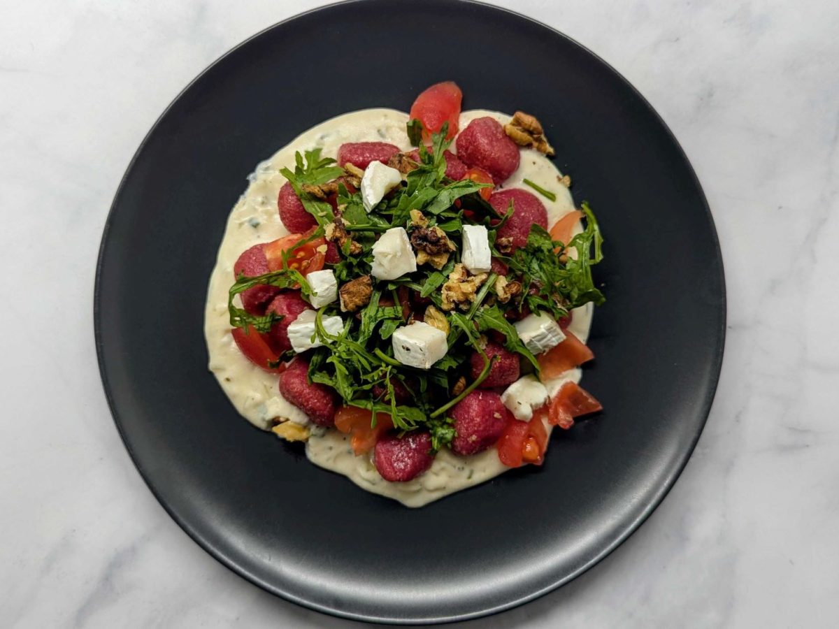 Rote-Bete-Gnocchi mit Frischkäse-Sauce und Rucola auf schwarzem Teller.